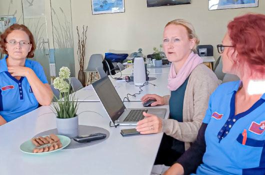 Auf dem Bild siehst du drei Pflegefachkräfte in entspannter Atmosphäre sich am Laptop im Team besprechen.