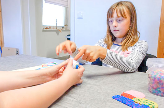 Auf dem Bild siehst du eine junge Patientin an einem bunten Übungsball bei einem Lernspiel mit ihrer Logopädin.