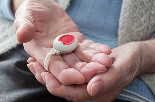 Hier siehst du einen tragbaren Notrufknopf an einem Band, den ein Senior in seinen Handflächen hält.