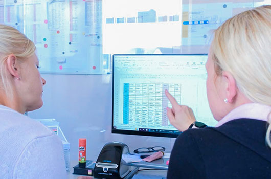 Auf dem Bild siehst du zwei Pflegerinnen die einen Wochenplan am Computer besprechen.