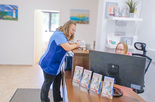 Das Bild zeigt eine Besprechungssituation zwischen zwei Fachkräften des Pflegeteam Behrens am Empfangstresen mit Informationsmaterial zum Mitnehmen.