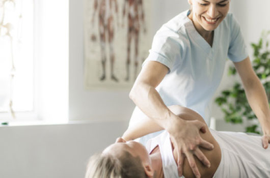 Das Bild zeigt eine Pflegefachkraft, die einem Patienten freundlich hilft, sich aus der Rückenlage auf die Seite zu drehen.
